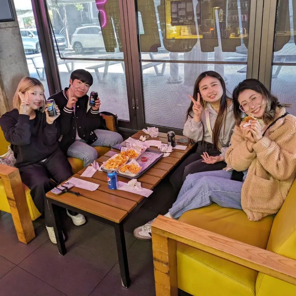 Four friends at a yellow booth inside Sneaky Burger Wollongong sharing fries and drinks